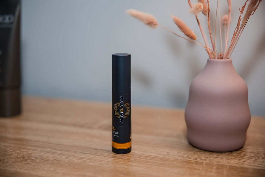 Brush on block tube standing on a wooden table, with a pink vase to the right 