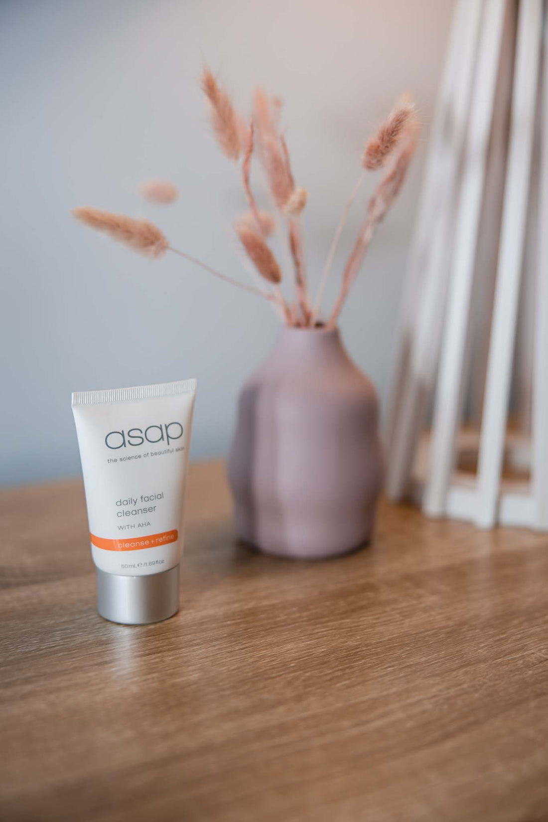 asap daily facial cleanser on a wooden table with a pink vase and table lamp to the rigth